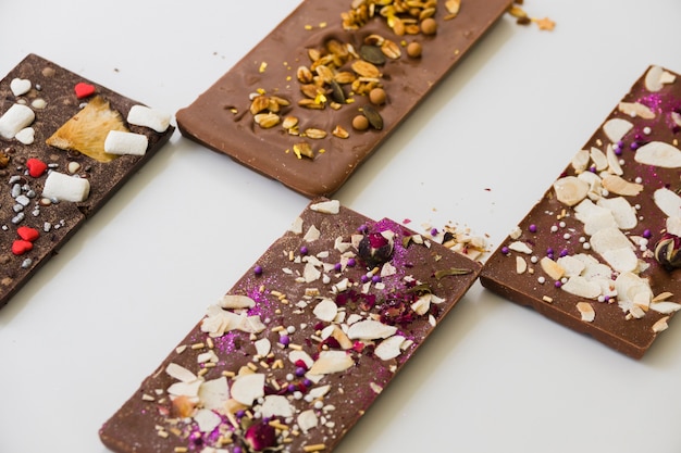 Chocolate bars with different toppings on white background