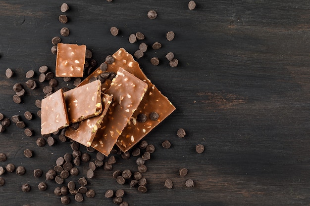 Chocolate bars with pistachio and choco drops top view on a dark background