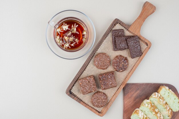 Chocolate biscuits, pistachio cake slices and glass of tea on white surface