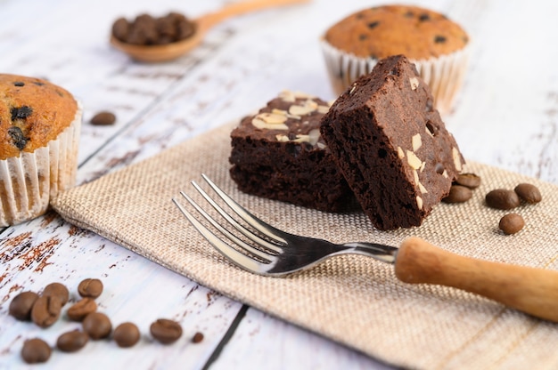 Chocolate brownies on sackcloth and coffee beans, fork on a wooden table.