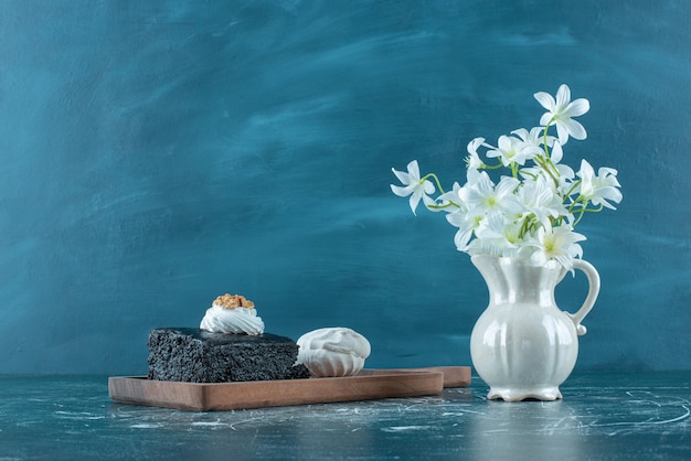 Chocolate cake, cookie and a vase of white lilies on blue.