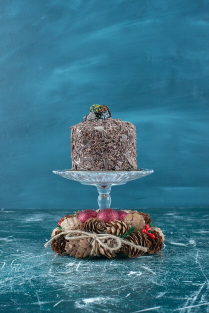 Chocolate cake on a pedestal and a pine cone wreath on blue.