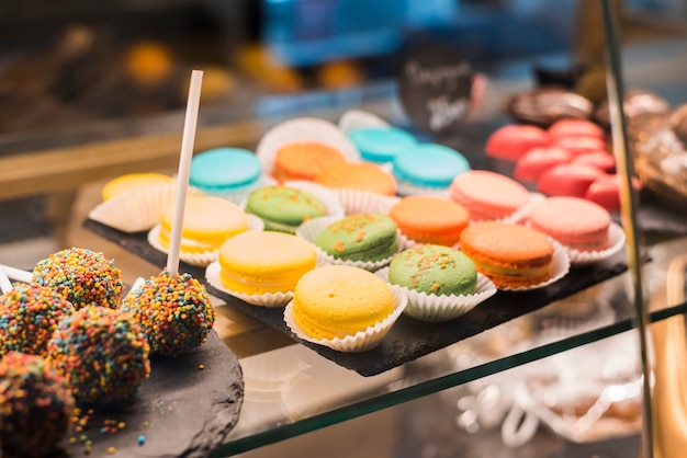 Chocolate cake pops with colorful sprinkles and macaroons in the display cabinet