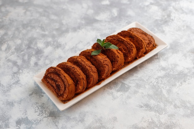 Free photo chocolate cake roll with cocoa powder on white plate,top view