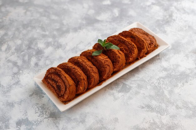 Chocolate cake roll with cocoa powder on white plate,top view