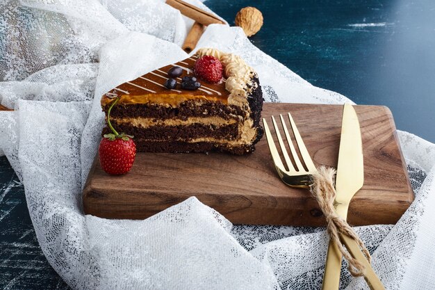 Шоколадный торт с клубникой на деревянной доске с набором столовых приборов.