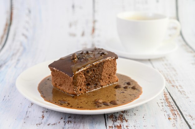 Chocolate cake topped with coffee on a white plate with coffee beans on a wooden table.