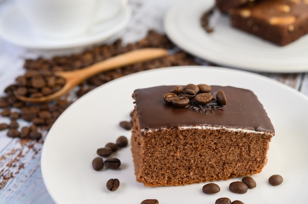 Chocolate cake on a white plate and coffee beans on a wooden spoon on a wooden table.