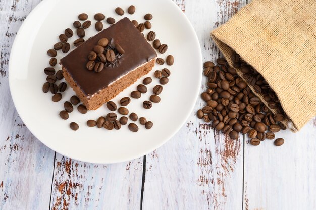 Chocolate cake on a white plate with coffee beans on a wooden table