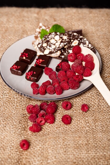 Chocolate candies and raspberry on white plate on sackcloth.