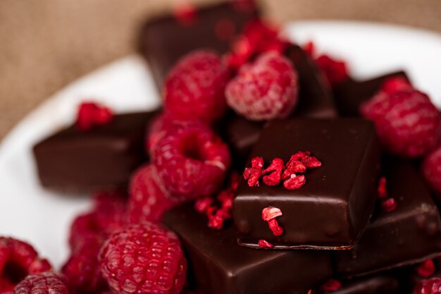 Chocolate candies and raspberry on white plate on sackcloth.