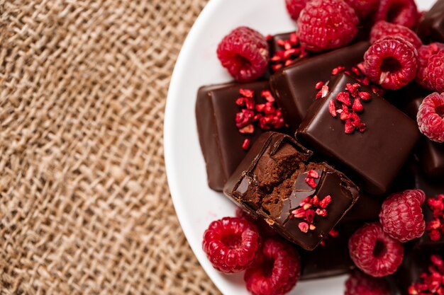 Chocolate candies and raspberry on white plate on sackcloth.