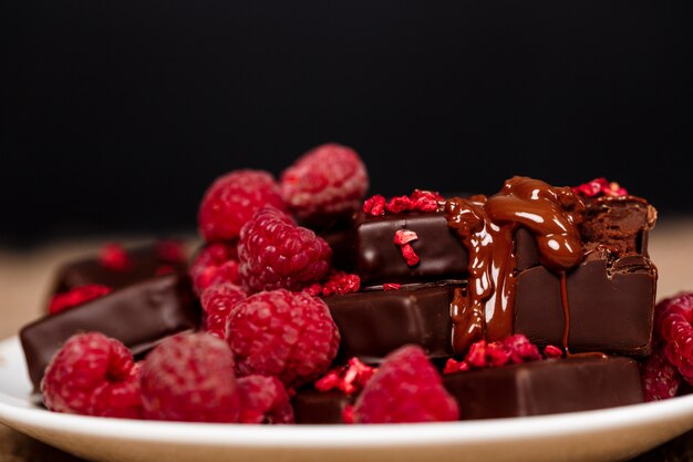 Chocolate candies and raspberry on white plate on sackcloth.