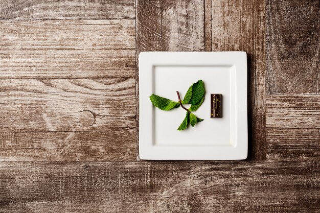 Chocolate candy and mint on white plate on wooden