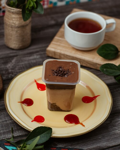 Chocolate caramel mousse in a plastic transparent cup with strawberry sauce and a cup of tea