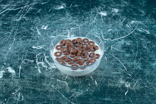 Anelli di fiocchi di cereali al cioccolato con latte in una ciotola di vetro, sullo sfondo blu. foto di alta qualità