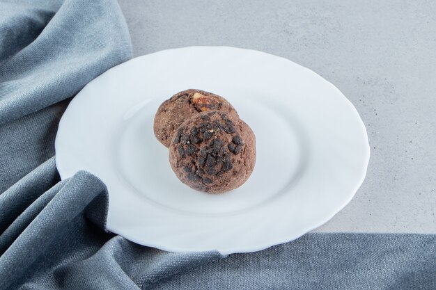 Chocolate chip cookies on a white platter next to table cloth on marble background.