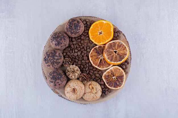 Покрытые шоколадной стружкой печенье, кофейные зерна и дольки апельсина на доске на белом фоне.