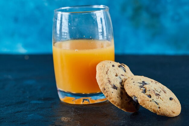 Chocolate chips cookies and a glass of orange juice on dark table