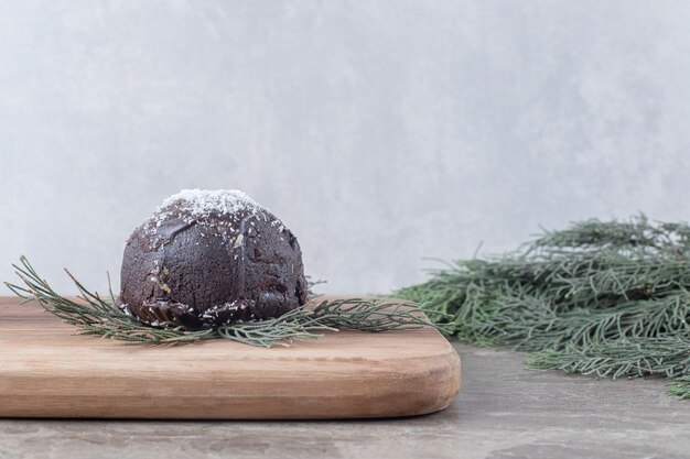 Chocolate coated cake, wooden board and pine branches on marble surface