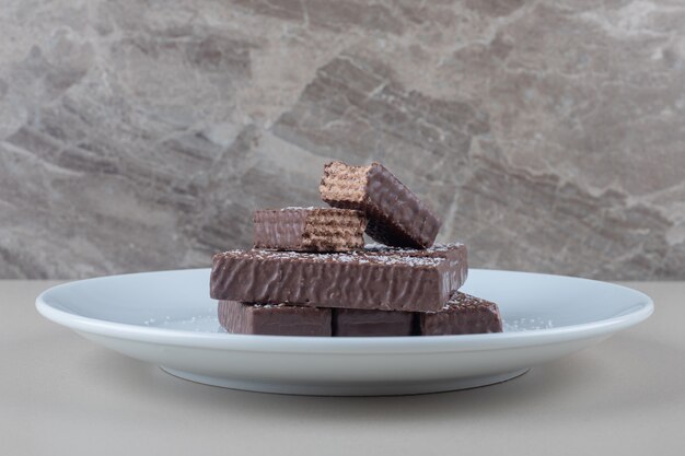 Chocolate coated wafers stacked on a white platter on marble background.