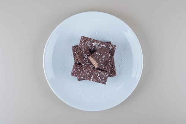 Chocolate coated wafers stacked on a white platter on marble background