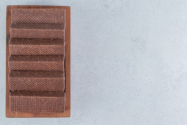 Chocolate coated wafers on a wooden platter on marble background.