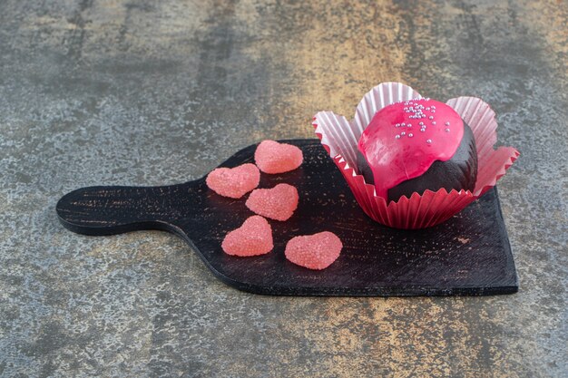 Chocolate cookie with pink glaze and candies on wooden board