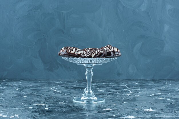 Free photo chocolate cookies on a glass pedestal, on the blue table.