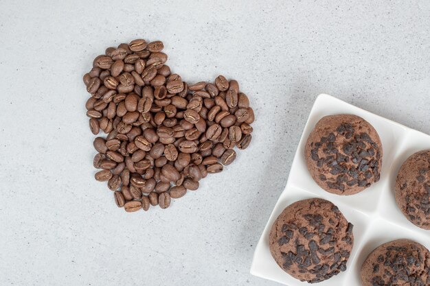 Chocolate cookies with coffee beans on white surface.