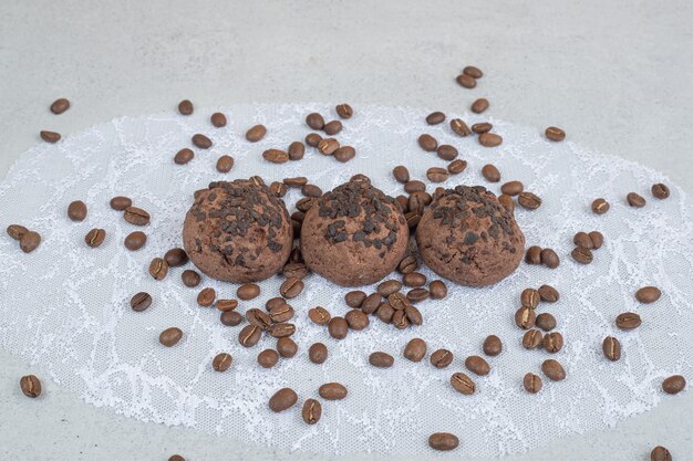 Chocolate cookies with coffee beans on white surface