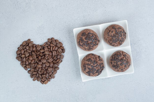 Chocolate cookies with coffee beans on white surface