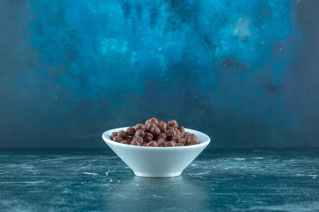 Chocolate corn balls in a bowl , on the blue background. High quality photo