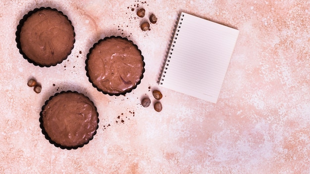 Chocolate cupcake; hazelnut and spiral notepad on textured background