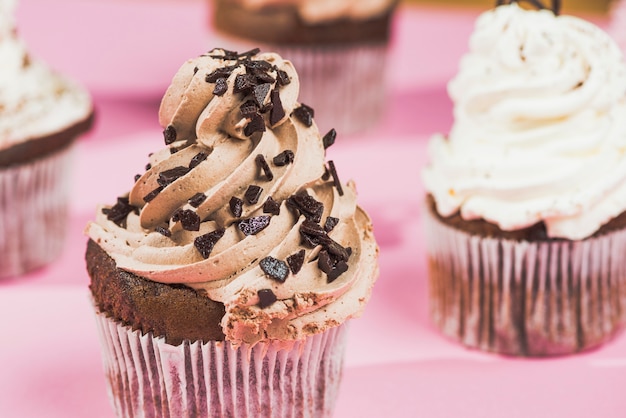 ピンクの背景に渦巻バタークリームとチョコレートカップケーキ