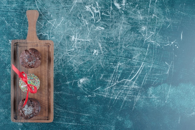 Chocolate cupcakes and a candy coated lollipop on a board on blue background. High quality photo