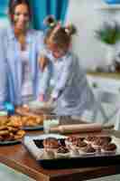 Foto gratuita tortini al cioccolato su un vassoio in cucina, nel muro mamma e figlia cuociono i biscotti