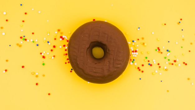 Free photo chocolate donut with colorful sprinkles on yellow background