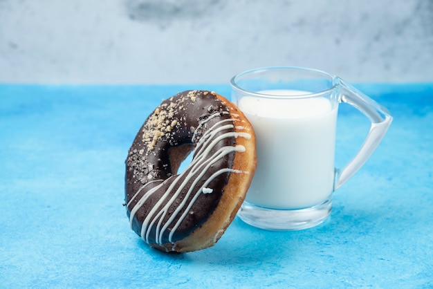 Foto gratuita ciambella al cioccolato con un bicchiere di latte sul tavolo blu.