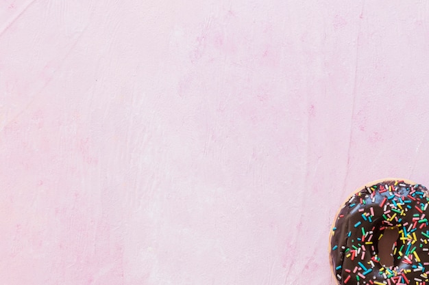 Chocolate donut with sprinkles at the corner of pink backdrop