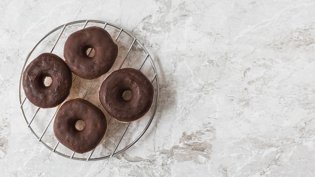 Chocolate donuts on metal rack over the marble textured backdrop