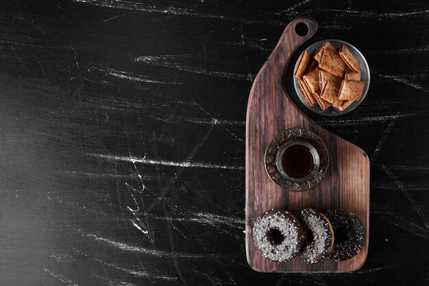 Chocolate doughnuts on a wooden platter with crackers around.