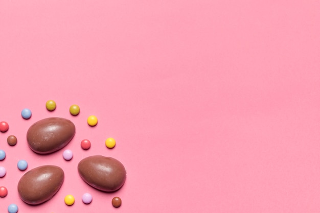 Бесплатное фото Шоколадные пасхальные яйца и драгоценные конфеты с копией пространства для написания текста на розовом фоне