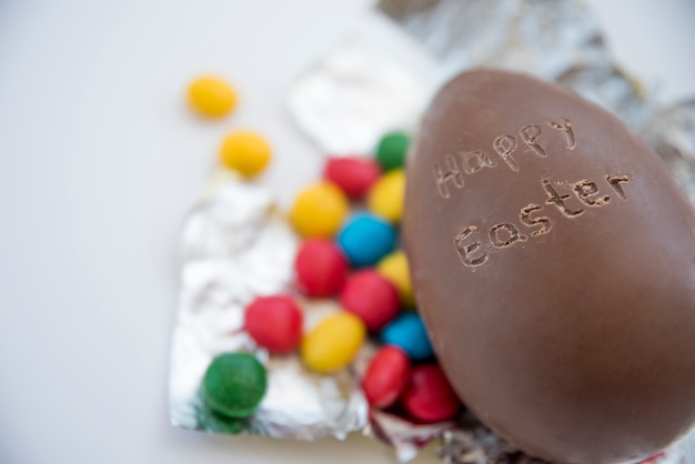 Foto gratuita uovo di cioccolato con felice titolo di pasqua e caramelle su carta stagnola