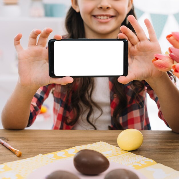 Шоколадные яйца перед девушкой, показывающей белый экран мобильного телефона
