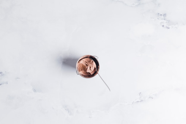 Chocolate ice cream in bowl with spoon on marble surface