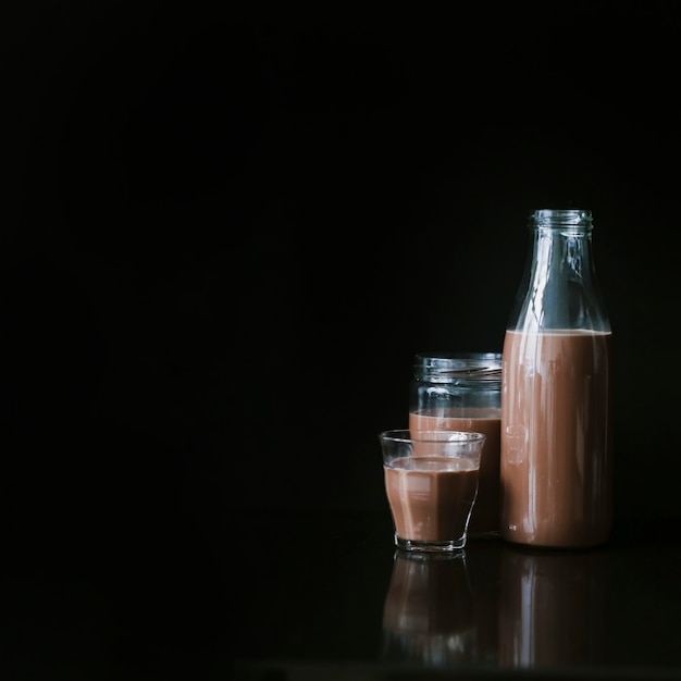 Chocolate milk shake in glass; jar and bottle on black background