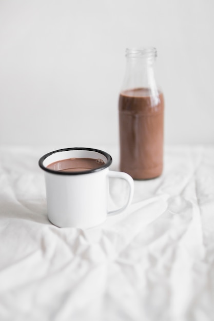 Chocolate milk shake in the white mug and glass bottle on table with white cloth
