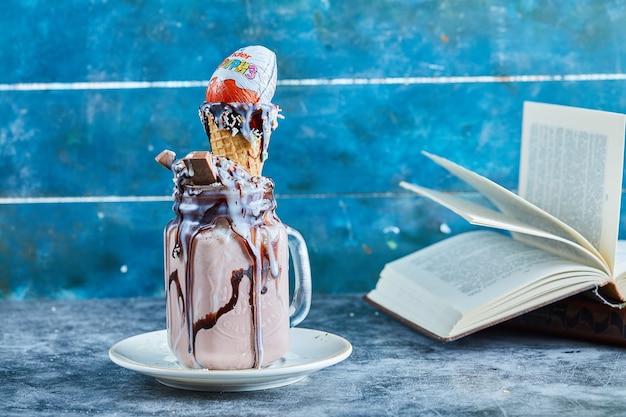 Chocolate milkshake with bar of chocolate, kinder surprise, ice-cream cone on the white plate 