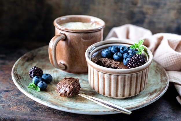 Free photo chocolate mousse with blueberries and blackberries and a cup of coffee on a dark background